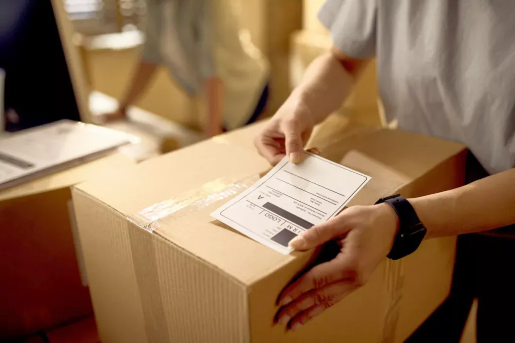 Hands placing a shipping label on a cardboard carton
